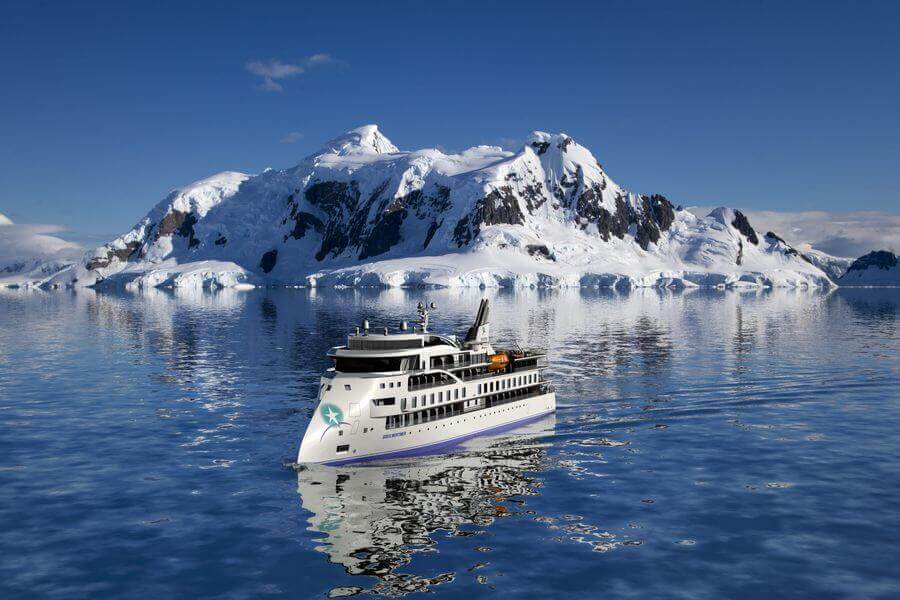 Greg Mortimer ship cruising past snowy mountains in Antarctica
