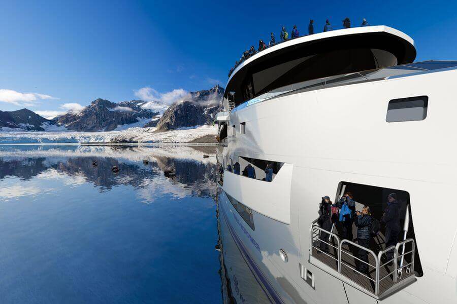 people looking out at Antarctica from the hydraulic platform of the Greg Mortimer ship